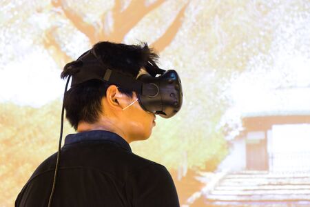 Asian teenager experiencing VR virtual reality entertainment gadget with screen background