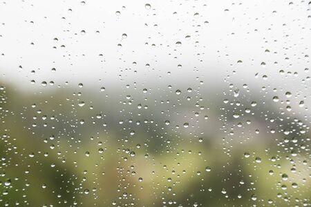 Rain water droplets on glass window with scenic greenery and gloomy sky view