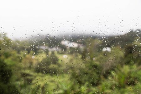 Rain water droplets on glass window with scenic greenery and gloomy sky view