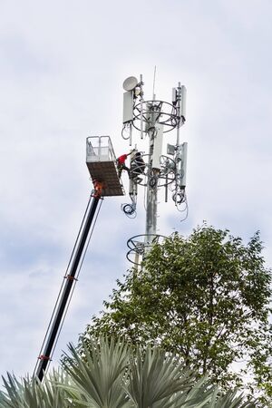Two workers on crane and protective harness installing mobile network communication antenna