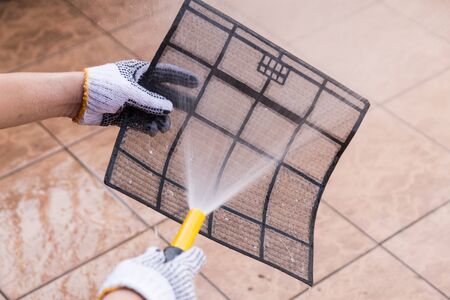 Person spraying water onto air conditioner filter to wash away thick dirty dustの写真素材