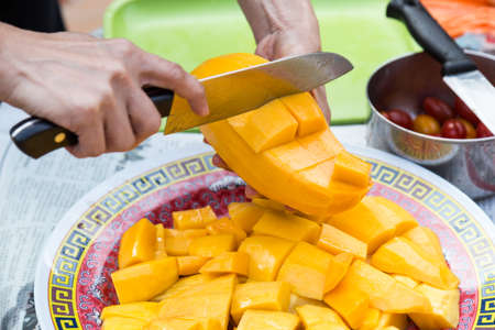 Hand holding knife cutting sweet delicious organic mango to serve on plateの写真素材