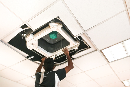Technician servicing, maintaining and fixing a ceiling air conditioner cartridge in officeの写真素材