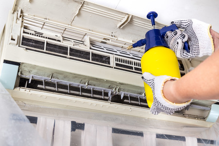 Technician spraying chemical water onto air conditioner coil to clean and disinfectの写真素材