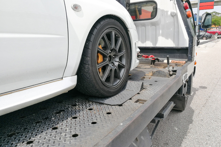 Broken down auto vehicle car towed onto flatbed tow truck with hook and chainの写真素材