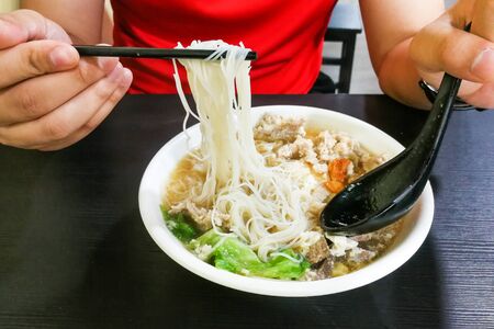 Person eating vermicelli pork noodle soup popular Chinese food in Penang Malaysia