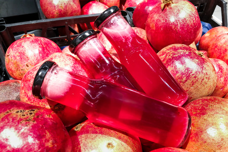 Fresh cold pressed organic pomegranate juice in bottle against heap of pomegranate fruitsの写真素材