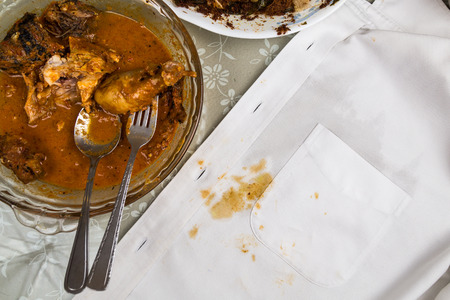 Plate of curry chicken and white shirt with curry stain accicently spilled.