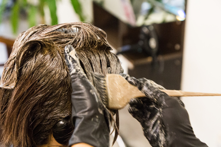 Closeup of hair dresser applying chemical color dye onto hair of customer in salonの写真素材