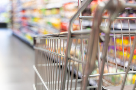 Shopping trolley cart with shallow DOF against modern supermarket aisle blurred background