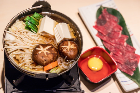 Japanese sukiyaki hot pot with vegetable, beef slice, raw egg served on tableの写真素材