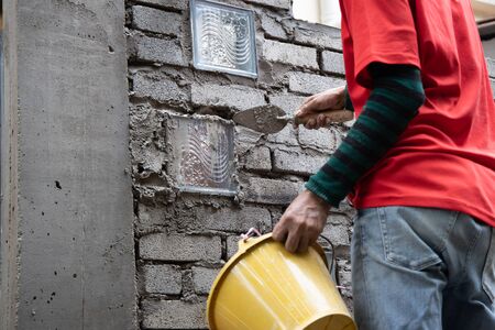 Asian worker installing glass block onto brick wall with mortar at construction site
