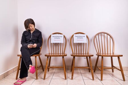 Asian woman seated next to chairs at public place, with Social Distancing, Do Not Sit signage, measure to prevent spread of Covid-19 pandemicの写真素材