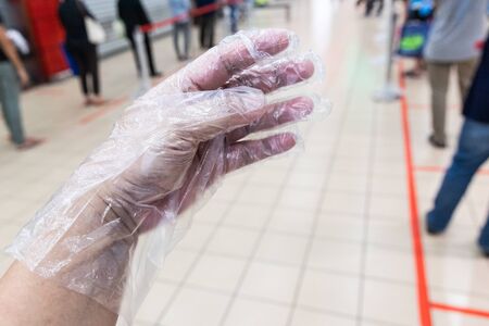 Person hand with disposable glove against background of people practice social distancing in queue into supermarketの写真素材