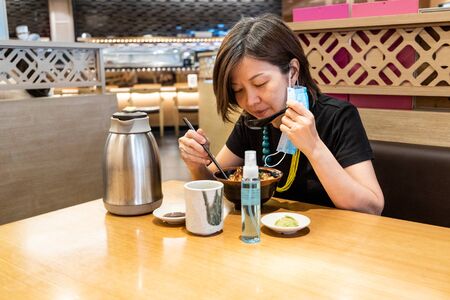 Asian women having meal with facemask and sanitazer, with social distancing in Malaysia