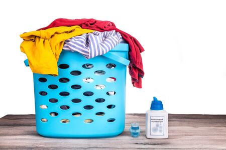 Compact concentrated laundry liquid detergent next to basket full of apparels on white background