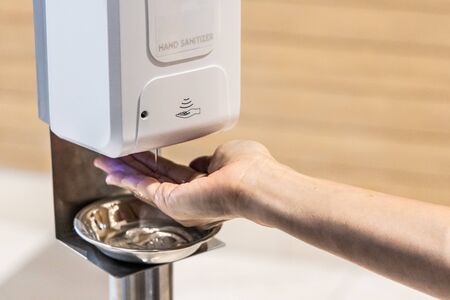 Person sanitizing hands with liquid gel from sanitizing machine in shopping mallの写真素材