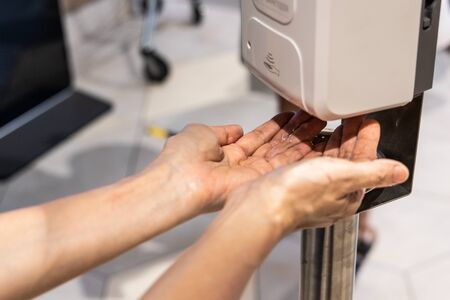 Person sanitizing hands with liquid gel from sanitizing machine in shopping mallの写真素材