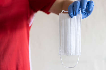 Hand with surgical gloves holding white face maskの写真素材