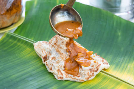 Curry being poured onto roti canai or paratha served on banana leafの写真素材