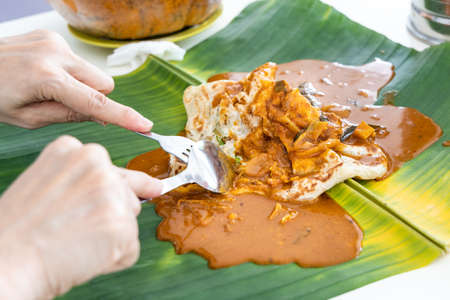 Person eating roti canai or paratha served with curry served on banana leafの写真素材