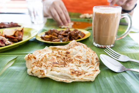 Roti canai or paratha served on banana leaf, with mutton curry and fried chicken, and popular teh tarikの写真素材