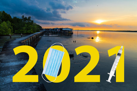 Welcome 2021 text against sunrise at seaside with face mask and syringe suggesting Covid-19...