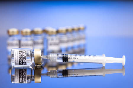 Syringe inserted into vial containing Covid-19 vaccine concept on blue background