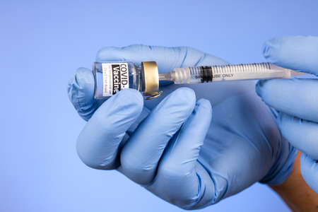 Close-up of hand with surgical glove insert syringe into covid-19 vaccine vial on blue backgroundの写真素材