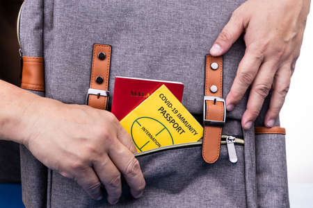 Conceptual of person placing Covid-19 Immune Passport and travel document into hand luggage pocket