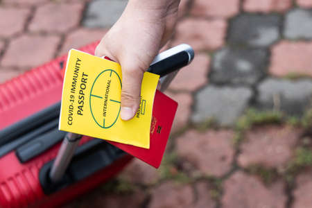 Traveller pulling luggage with conceptual Covid-19 Immunity Passport on handの写真素材