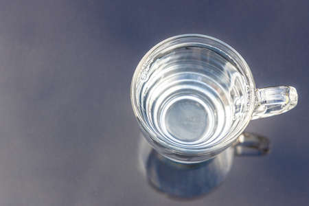 Still clean drinking water in transparent glass on surface reflected against blue sky and cloudの写真素材