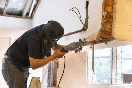 Worker drilling on wall to create cavity for electric power cables in home renovationの写真素材