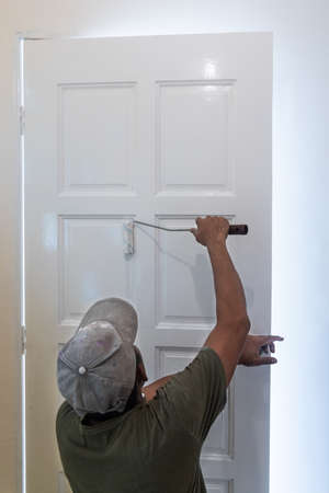Person painting wooden white door with paint roller during home rennovationの写真素材