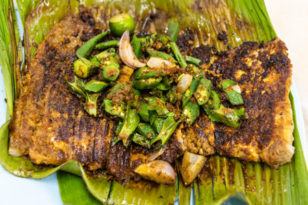 Close-up overhead view of grilled stingray fish with spices topped with okra vegetable on banana leaf popular street food in Malaysiaの写真素材