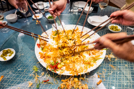 People mixing and tossing yusheng or yee sang during Chinese New Year dinner celebration, believed to bring luck. Slow shutter speed with motion blur intended.の写真素材