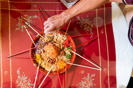 Hand pouring ingredients onto a serving of yusheng or yee sang with raw salmon belly during Chinese...
