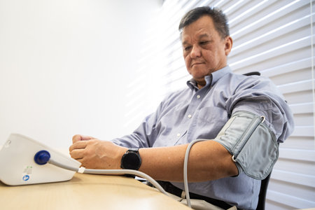 Stressful Asian man in 50s checking blood pressure with instrument in the work office