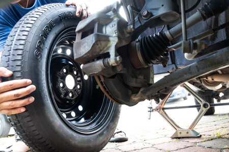 Person attempting to fix or replace temporary spare tire wheel onto vehible after omiting punctured...