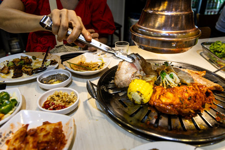 Delicious korean barbeque meal with pieces of beef, pork, chicken placed onto mesh to grill, with condiments and vegetables in restaurant.の写真素材
