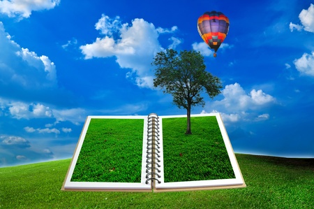 Open book with tree and hot air balloon over green field and blue skyの写真素材
