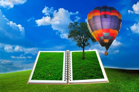 Open book with tree and hot air balloon over green field and blue skyの写真素材