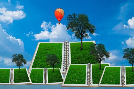 Open book with tree and hot air balloon over green field and blue skyの写真素材