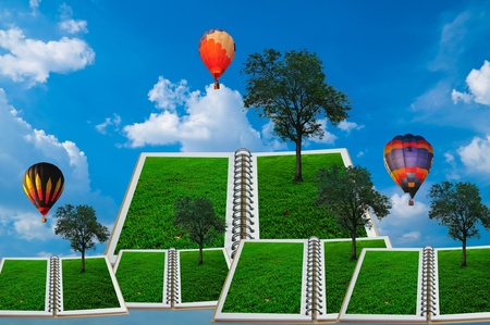 Open book with tree and hot air balloon over green field and blue skyの写真素材