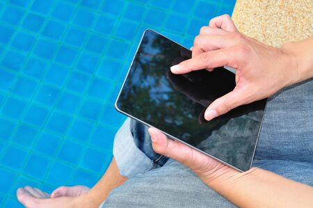 businessman working on PC tablet with feet in the pool の写真素材