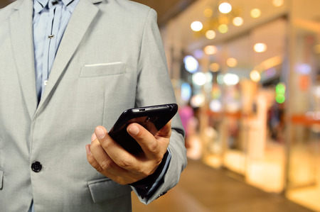 Handsome young man in shopping mall using mobile phone.  Selective focus on Phone and Hand.の写真素材