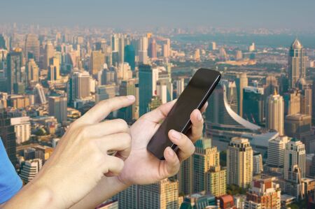 Hand of Young adult Tourist use Mobile Device smartphone over City Building Backgroundの写真素材