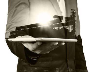 Double Exposure of Businessman with Tablet wireless Device and Silo Plant or Warehouse as Business Technology Conceptの写真素材
