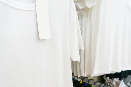 blank price tag hang over white tshirt on Hanger Shelf in Supermarket or Hypermarket Retail Store Outlet, Shallow Depth of Field.の写真素材
