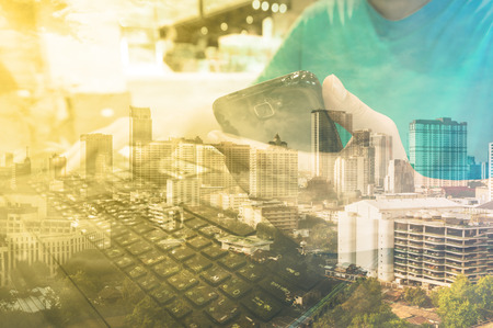 Businessman using Smartphone and Laptop Computer in cafeteria, Double Exposure with City Building.の写真素材
